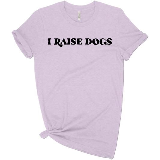 A soft beige “I Raise Dogs” t-shirt folded neatly with a paw charm beside it, styled for dog moms and pet lovers.